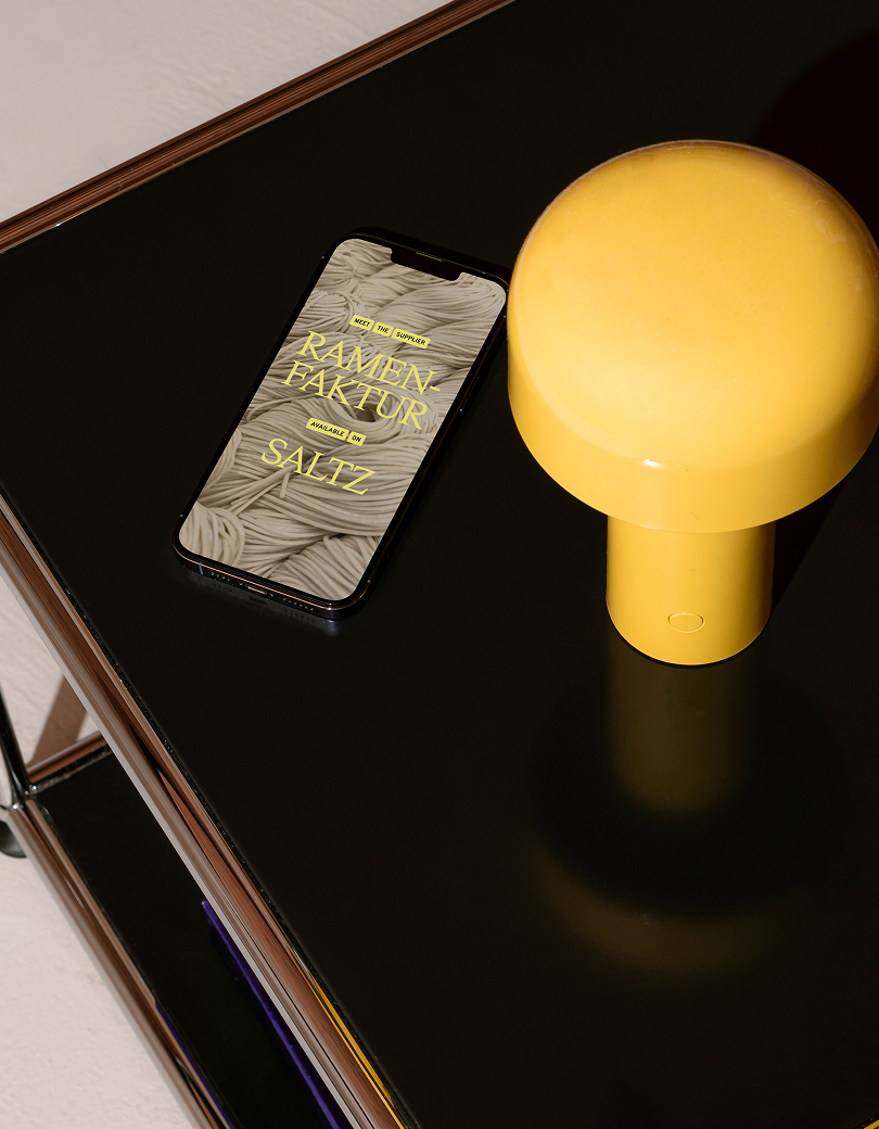 Phone showing a Saltz concept beside a yellow lamp